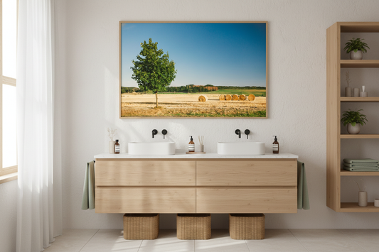 A single green tree stands beside golden hay bales in a sunny summer field under a clear blue sky