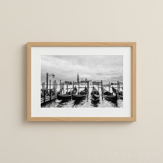 Framed black and white photograph of gondolas on a canal with a cityscape in the background.