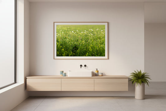 Modern bathroom with wooden vanity, sink, and framed picture of a green field.