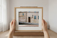 Load image into Gallery viewer, Person holding a framed picture of a building with a white wall and wooden frame.
