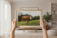 Load image into Gallery viewer, Framed picture of a cow in a field held by hands in a room with decor.
