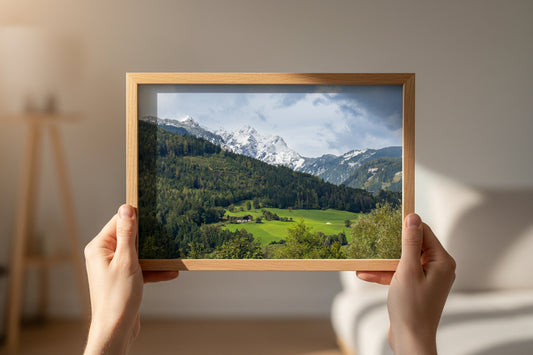 Framed picture of a mountain landscape held by hands against a neutral background